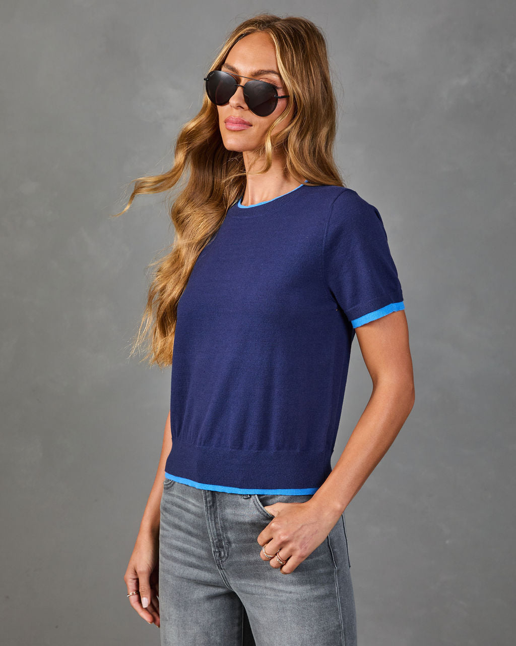 Navy blue short-sleeve knit sweater top with bright blue contrast trim at neckline, sleeves, and hem, styled with gray jeans