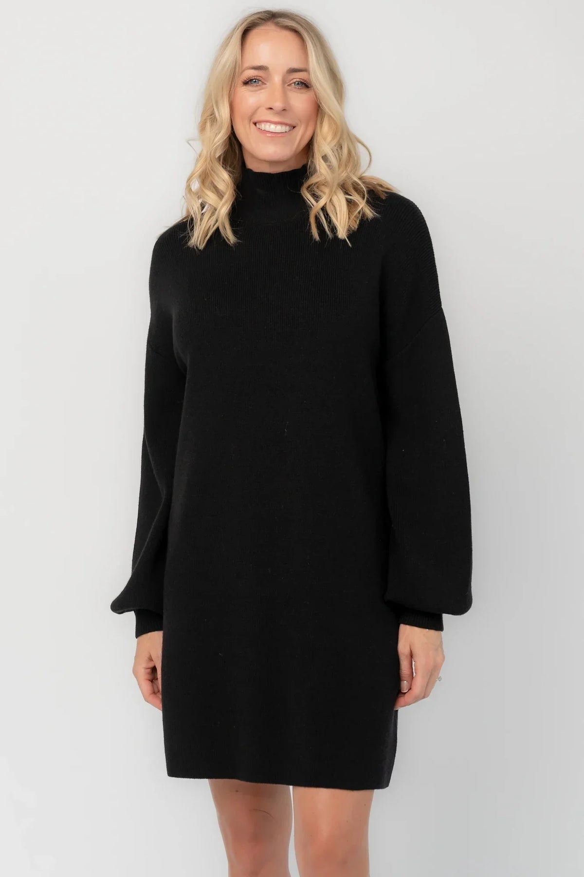 Black knit sweater dress with a mock neckline, long balloon sleeves, dropped shoulders, and a relaxed above-the-knee silhouette.